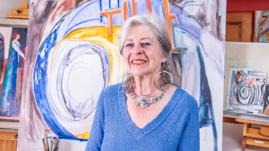 older woman in blue smiling while standing in front of artwork