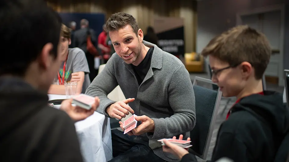 Joshua Jay demonstrates a card trick to children at a table