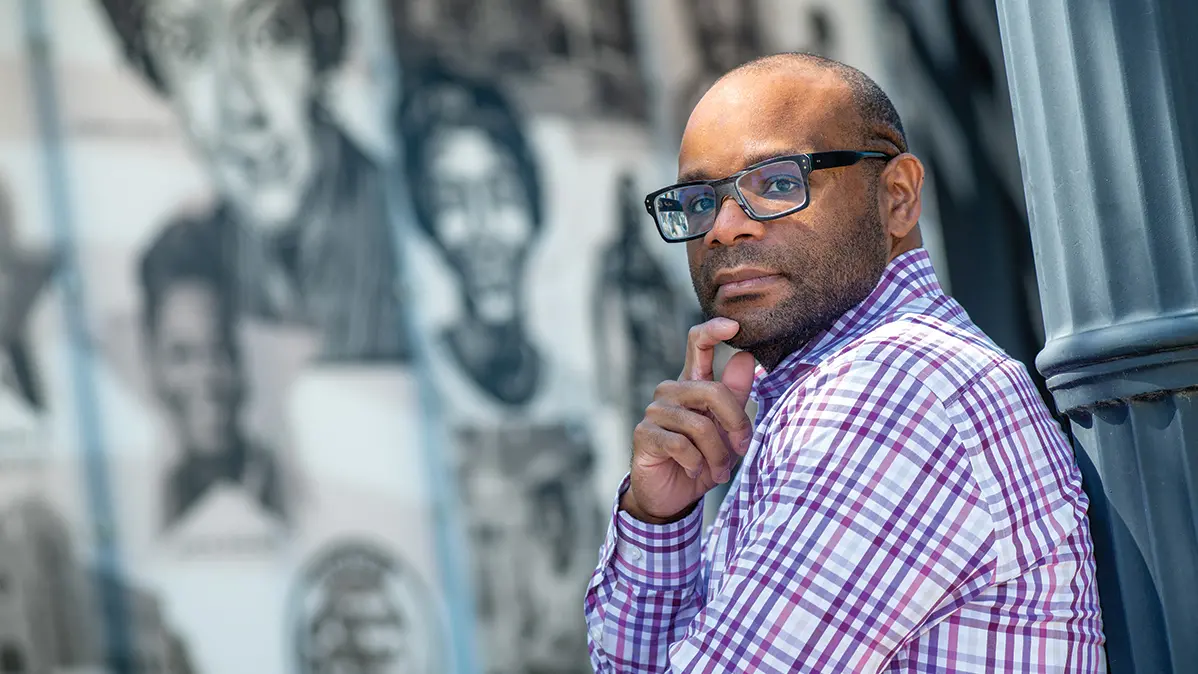 Headshot of Trevon Logan, bald Black man with glasses, wearing checked button up shirt