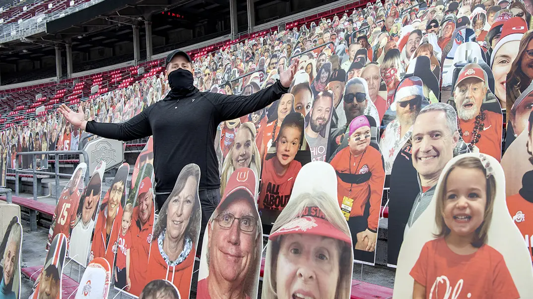 A man is standing amongst life-sized cutouts of fans positioned in the seats of Ohio Stadium
