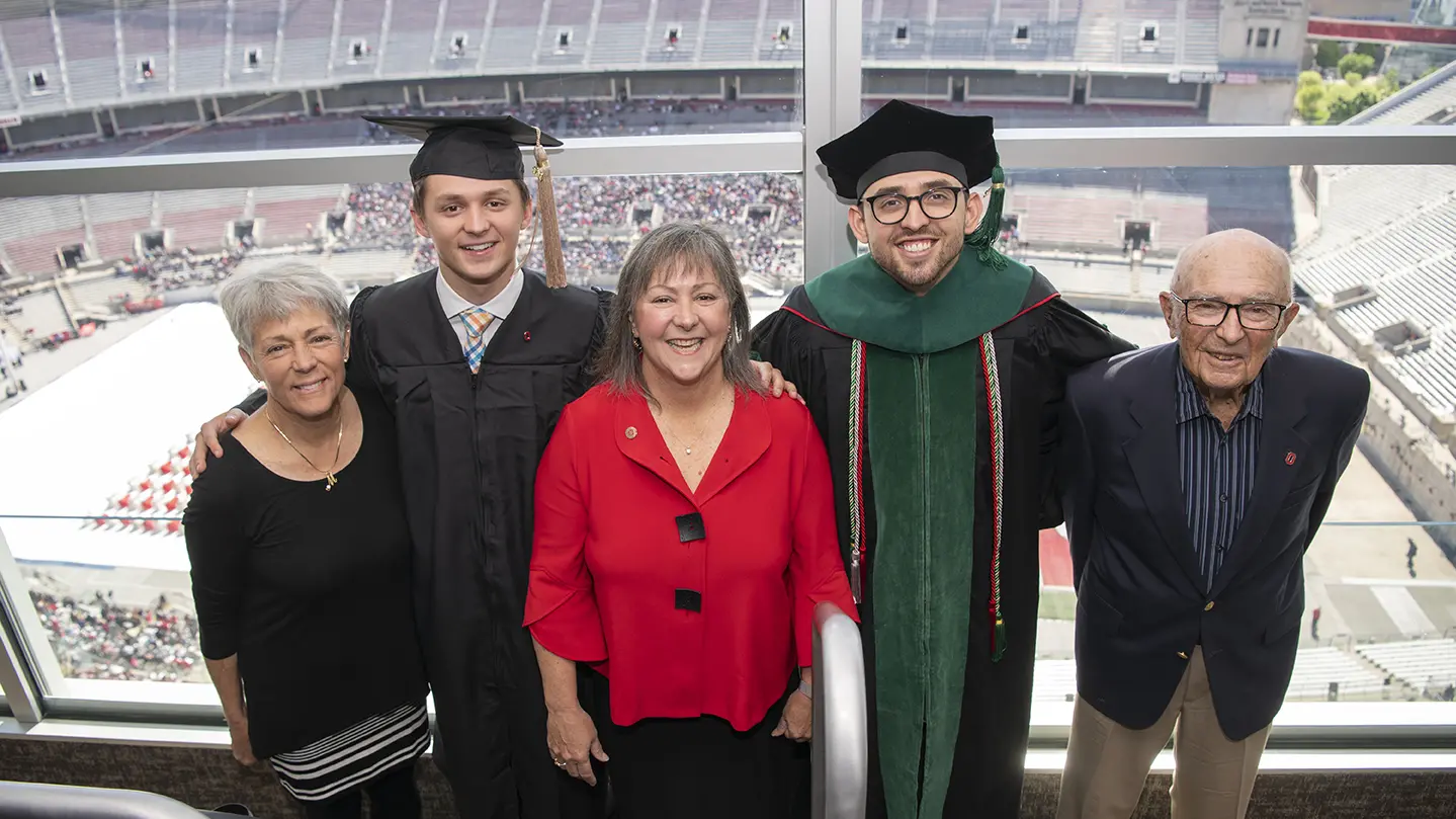 In a photo of a family, two young men wear graduation caps, gowns and smiles, as their mom, aunt and grandpa stand proudly by their sides.