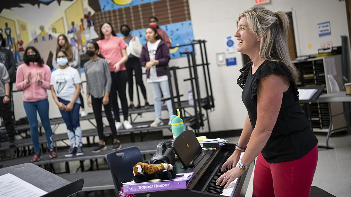 Katie Silcott plays electric piano in her classroom surrounded by students singing