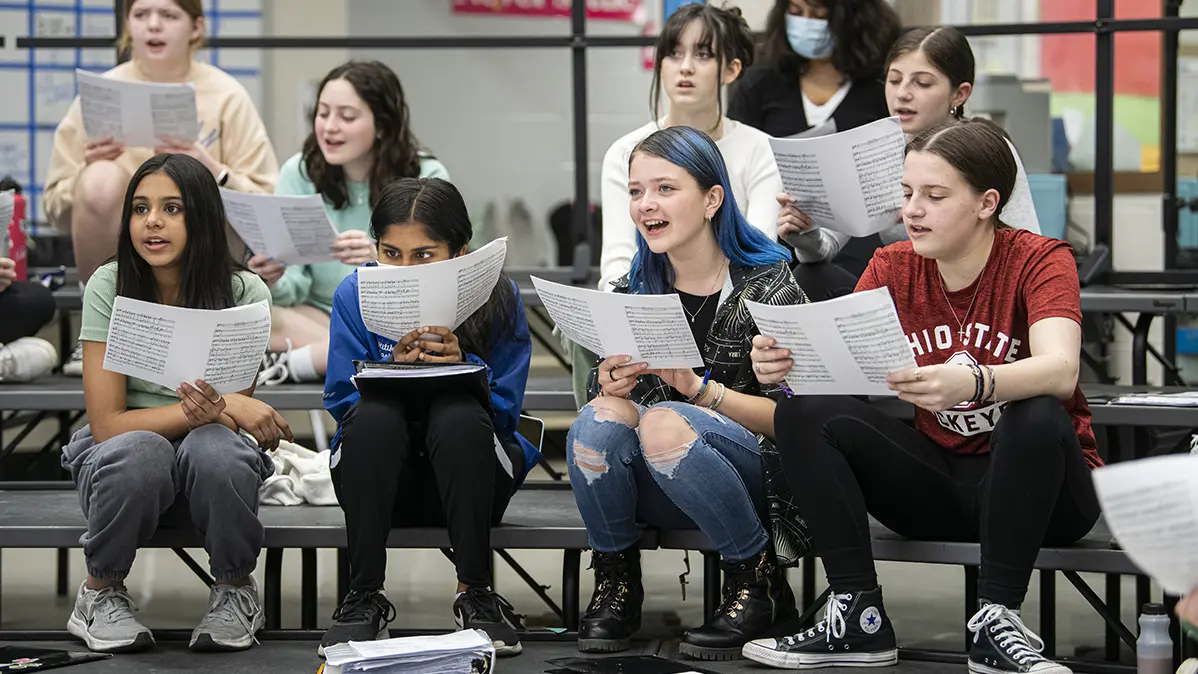 Students sit on bleachers singing in class