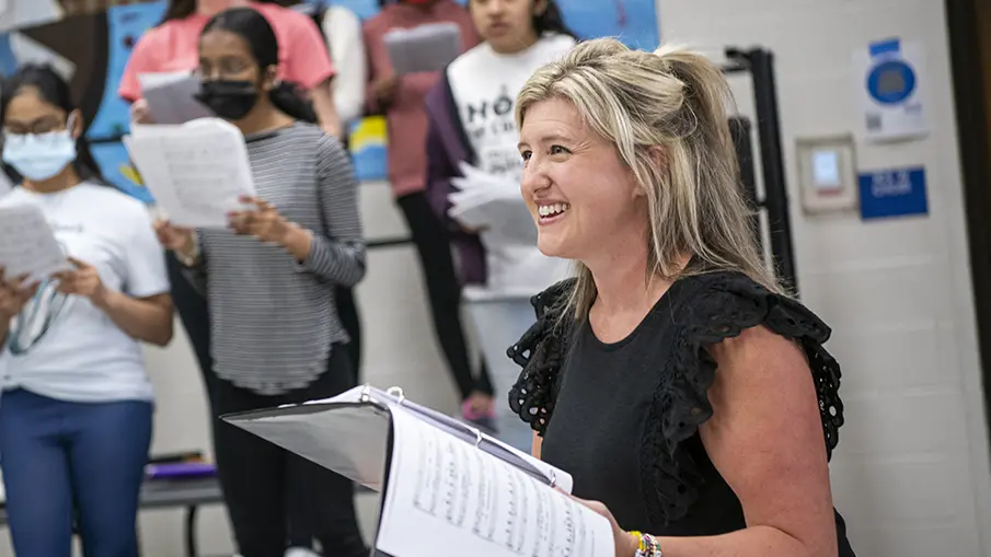 Katie Silcott holds sheet music leading class of students singing