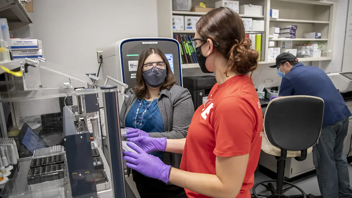 three people in a lab setting wearing personal protection equipment