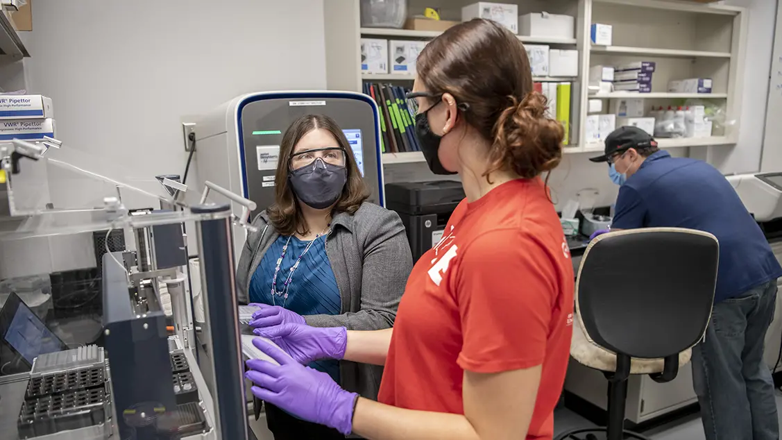 three people in a lab setting wearing personal protection equipment