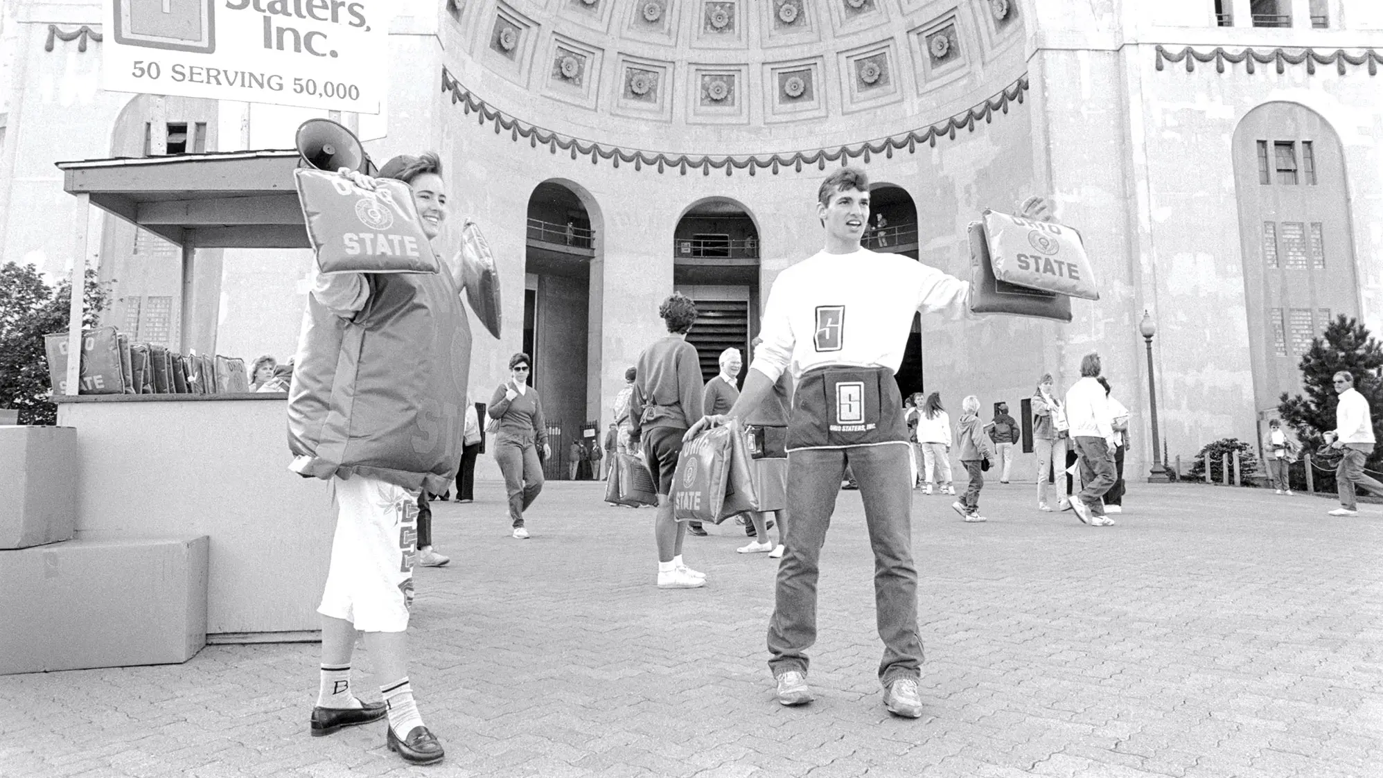 man and a woman handing out seat cushions to spectators in front of ohio stadium