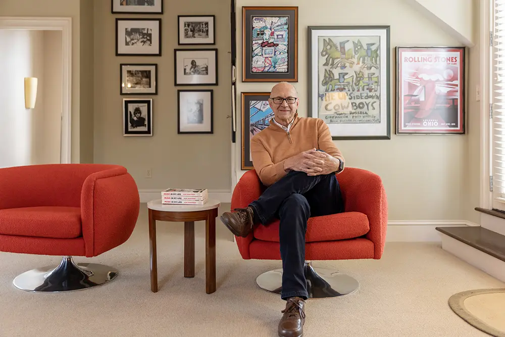 Relaxed and quietly happy, a man sits in front of music photos and posters.