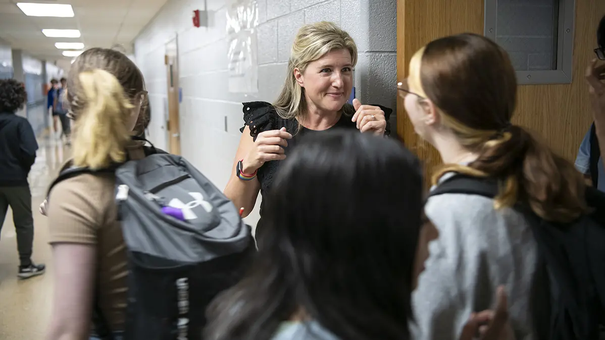 Katie Silcott talks with a student in a busy school hall.