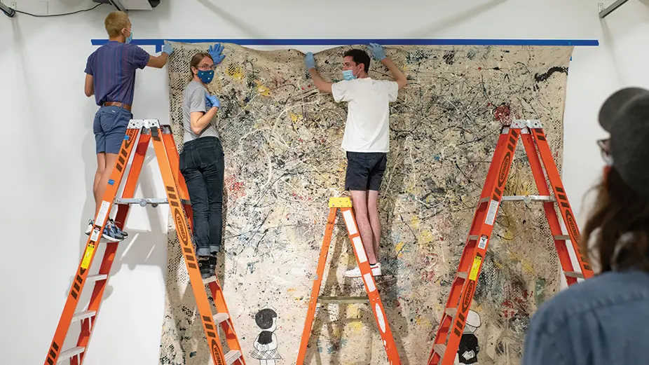 three people standing on ladder working on art piece