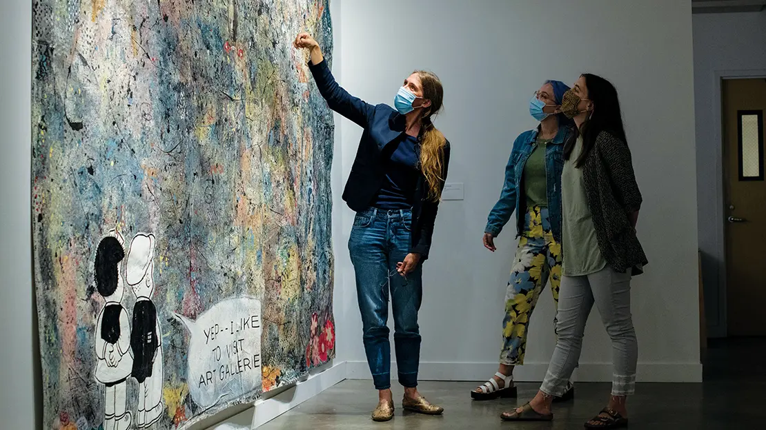 woman discusses a painting with two students