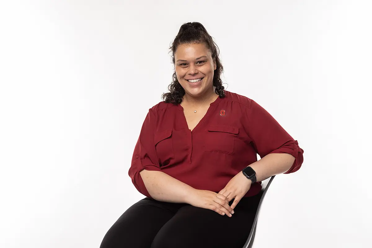 A biracial woman with a friendly smile poses on a chair.