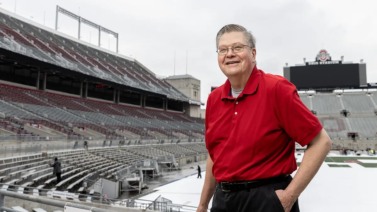 An older man stands in Ohio Stadium looking proudly into the camera.