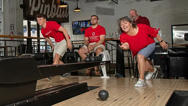 Molly throws a duckpin bowling ball down the lane. Her husband and two sons are in the background