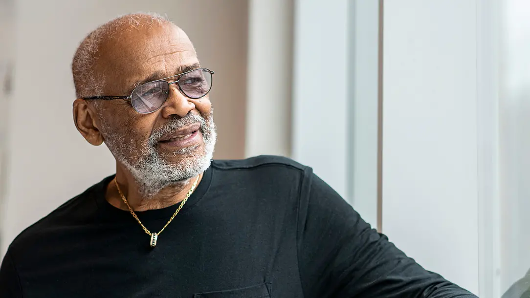 An older black man with gray hair and glasses seems thoughtful as he looks into the distance.