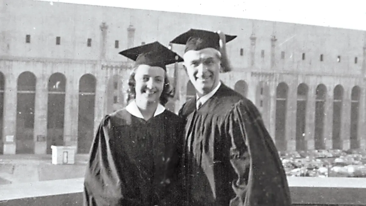 Both in cap and gown, a father and daughter proudly pose in front of Ohio Stadium.