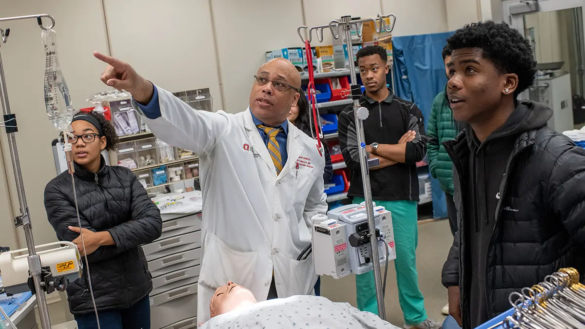 Dr. Quinn Capers demonstrates a virtual surgery suite for students from Eastmoor Academy High School. He points to a monitor that relays the vital signs to medical students studying in the lab.
