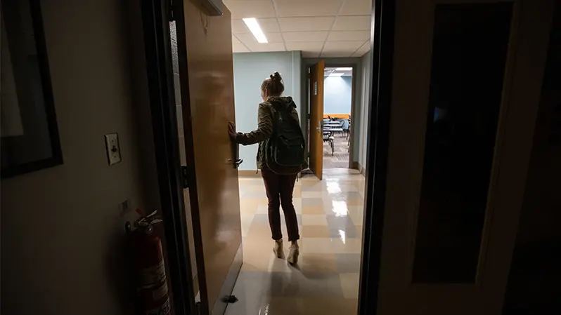 Student wearing a backpack walks through dark hallway