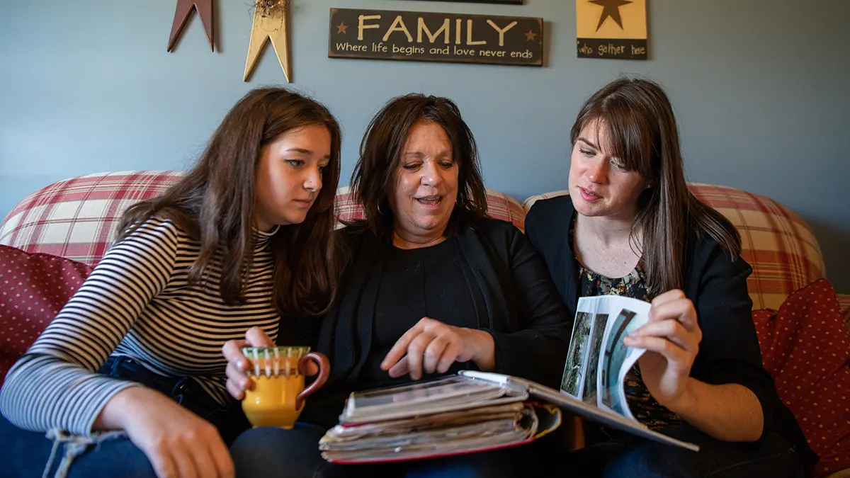 two sisters and their mother reminisce over a family photo album