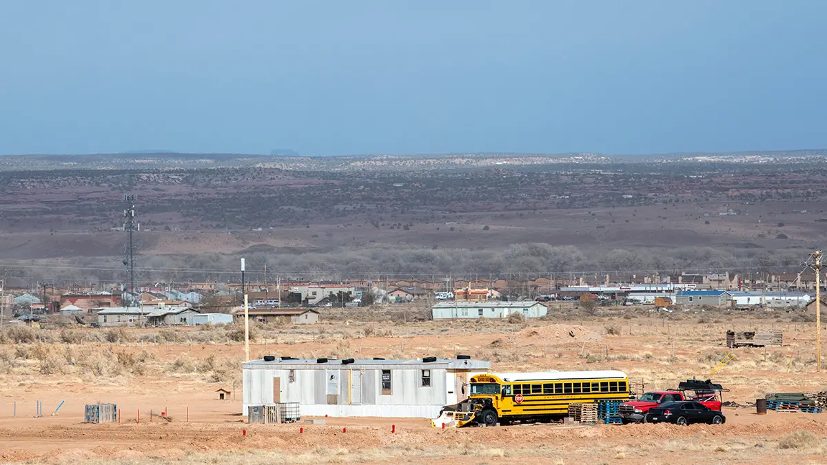 A school bus is parked next to a trailer in the distance. Farther beyond are a number of similar homes.
