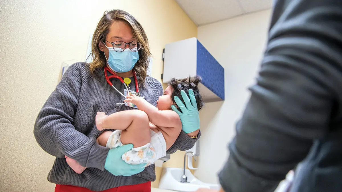 A young doctor cradles a baby wearing a diaper in an exam room