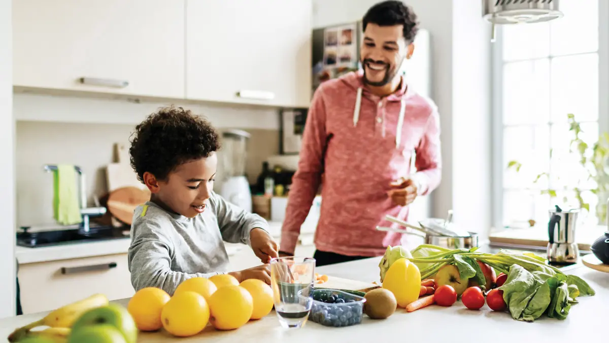 A father and son enjoy preparing fruits and vegetables at the island in their kitchen.