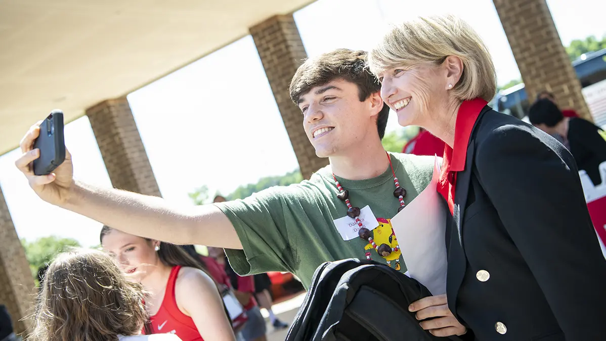 Ohio State President Kristina M. Johnson, a white woman with short blond hair, smiles and poses for the camera with a student