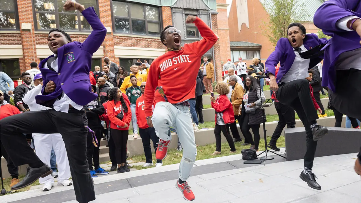 Several young Black men dancing in step and have big smiles and animated expressions