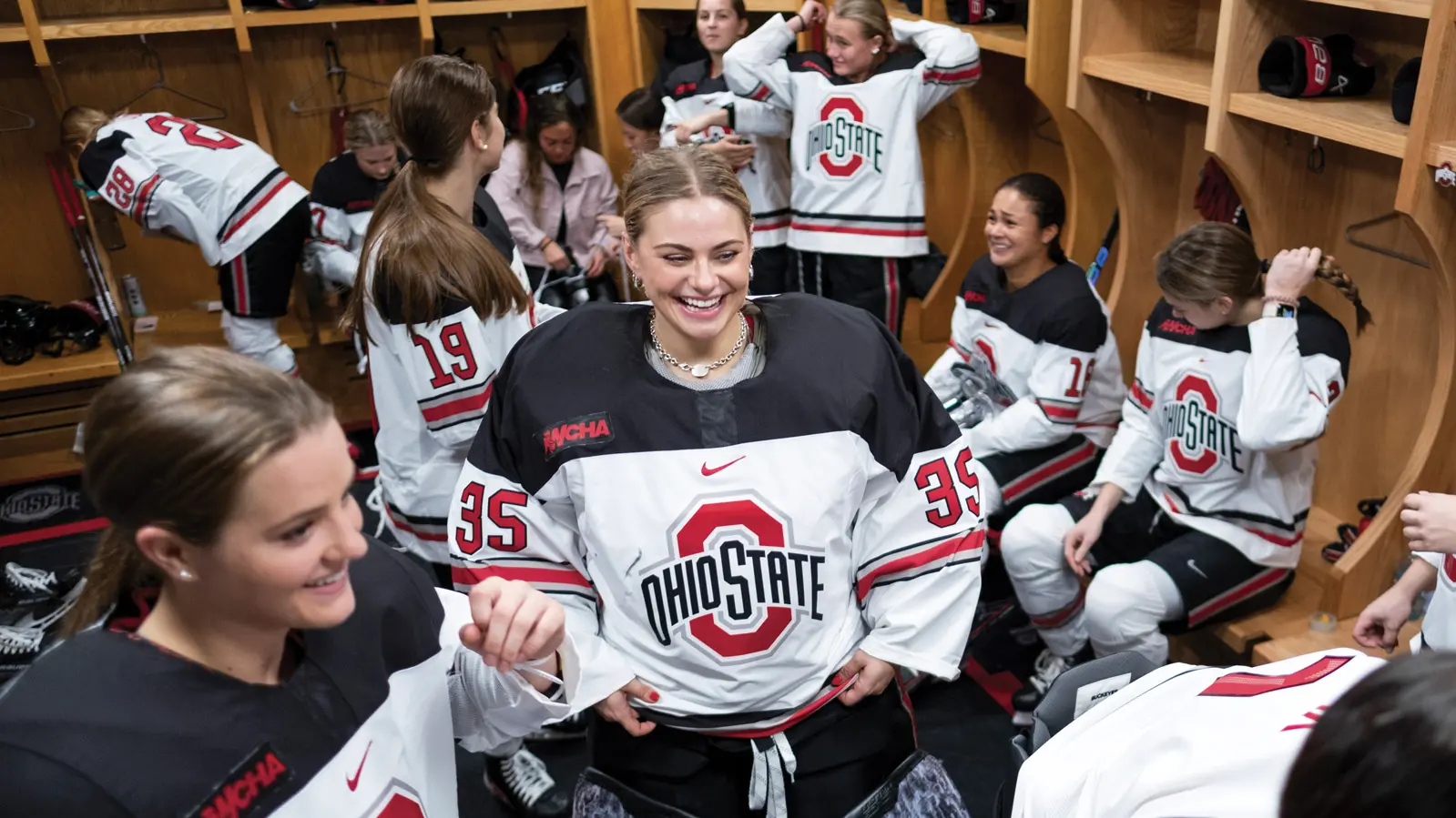 In a crowded locker room, young women in ponytails and Ohio State hockey uniforms laugh and talk in groups.