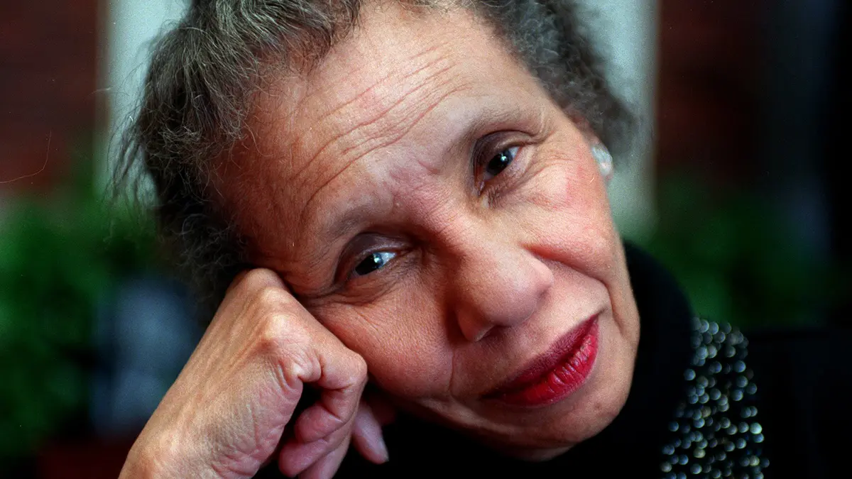 A portrait of Adrienne Kennedy gives a close-up view of an attractive black woman whose smiling eyes show her wisdom and her face, her years, as she leans her head on her hand. She’s wearing lipstick on her quietly smiling lips, a black turtleneck sweater with embellishments but no nail polish. Because of the way the photo is shot, her face is very in-focus but the background and her clothing become just hints of color and pattern.