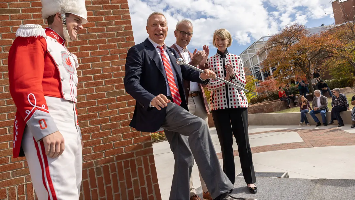Two Ohio State leaders and the band’s drum major stand outside the new music building, laughing as their companion, Ratmir Timashev, grins and pretends to be a marching drum major, having borrowed his baton. The leaders and Timashev wore suit coats for the special occasion.