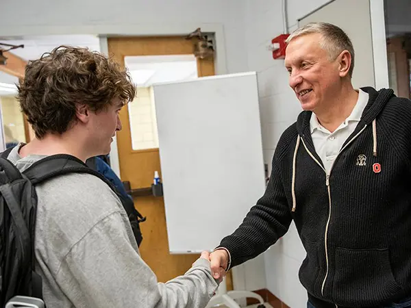 Ratmir TImashev, a man wearing a friendly smile and Ohio State zip-up, shakes hands with an Ohio State student in a classroom work space.