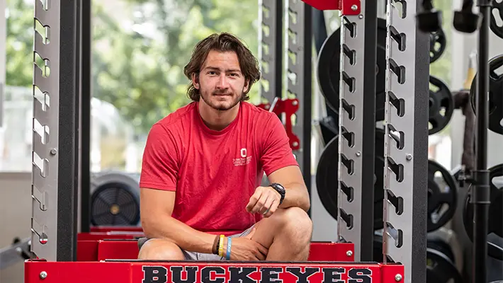 Anthony Dujmovic, a young man in a T-shirt and shorts, looks straight into the camera with a slight smile. His pose and expression make him seem confident and smart.