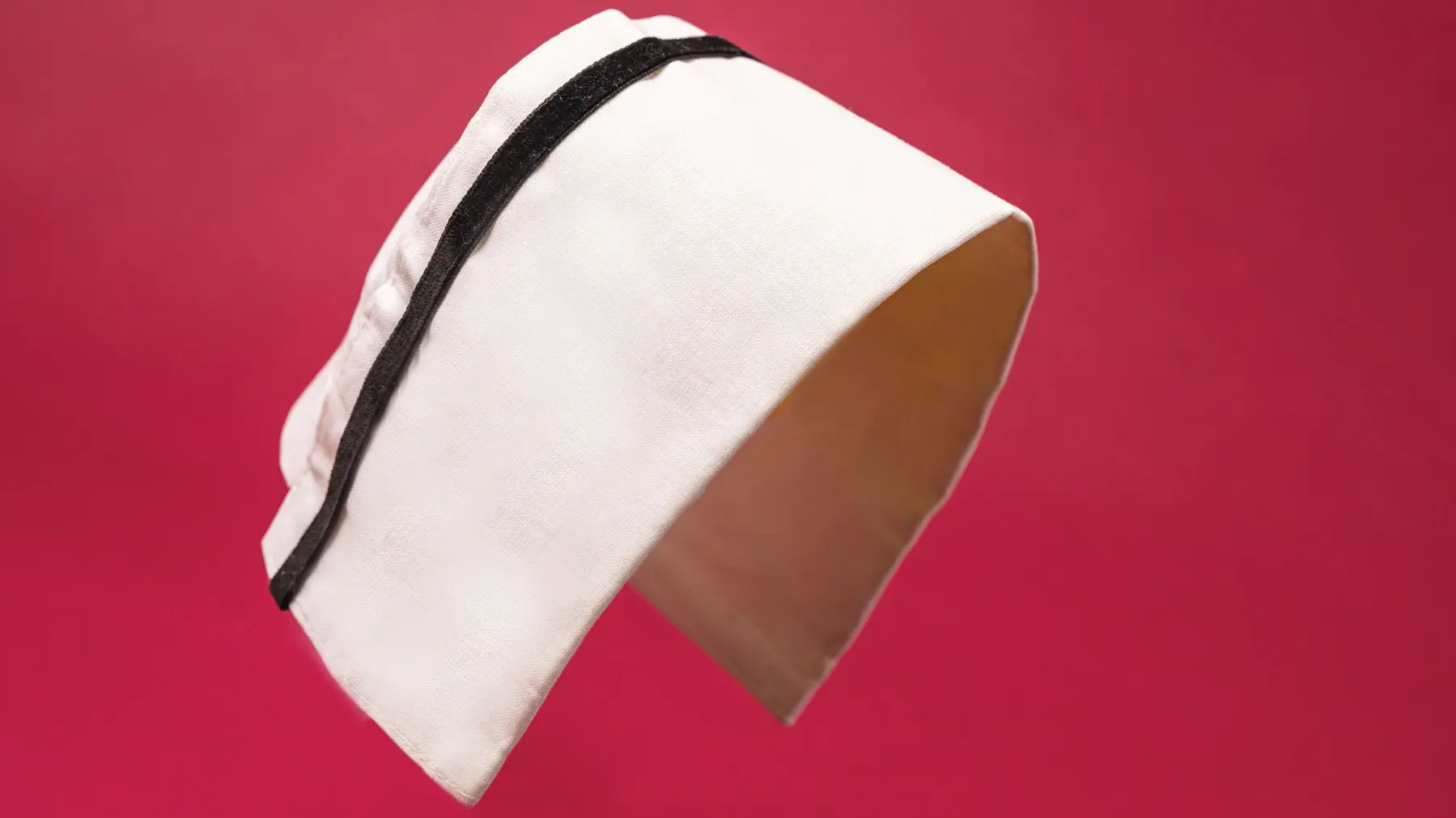 A whiteish rectangle of fabric, with a black velvet ribbon a quarter of an inch from the top, is shown arched as if on top of a nurse’s head.
