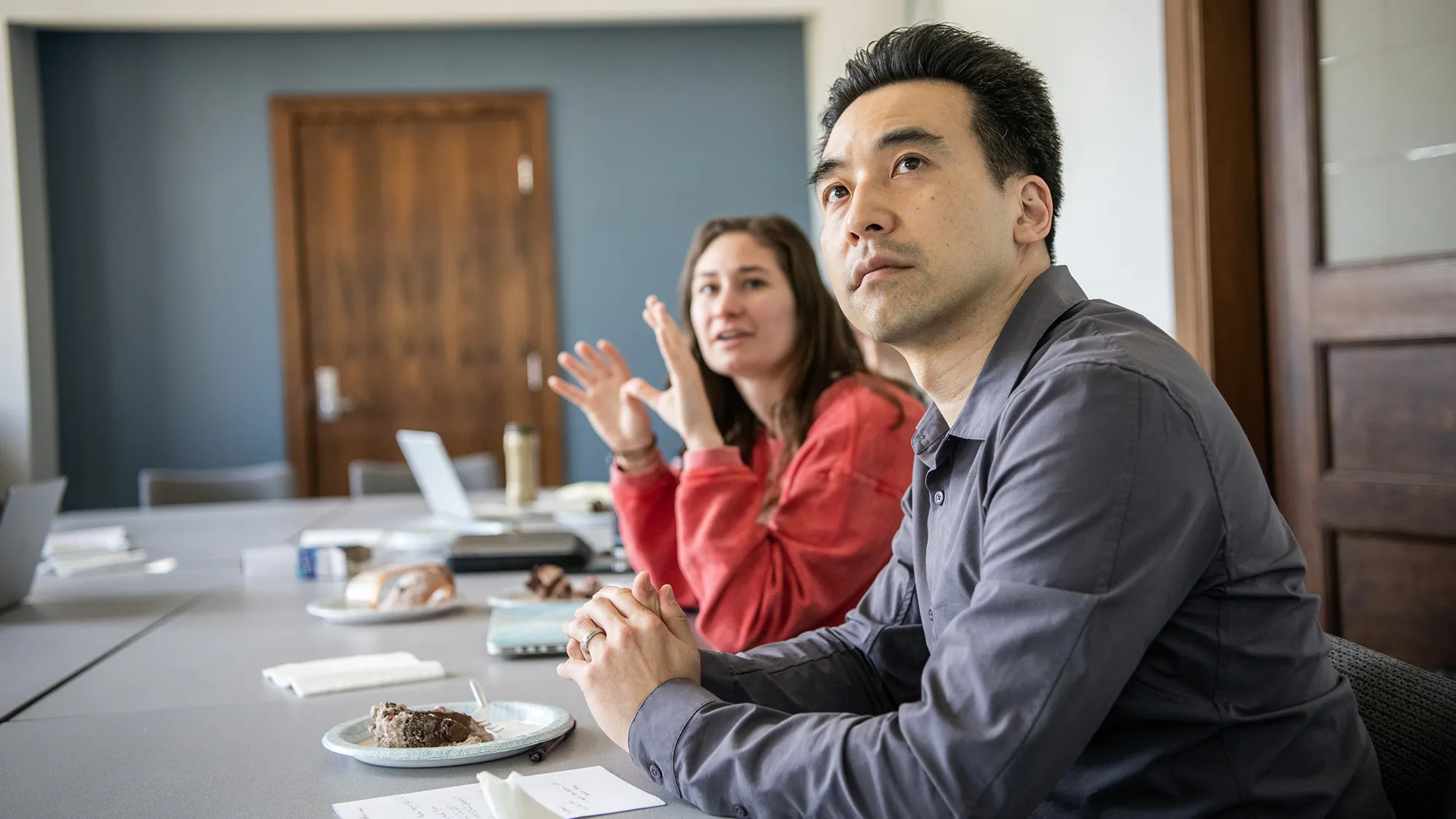 Kentaro Fujita, an Asian man, focuses on a slide show being shown out of the photo frame, as a student, a young white woman with long hair, next to him gestures as she explains a point of her project.