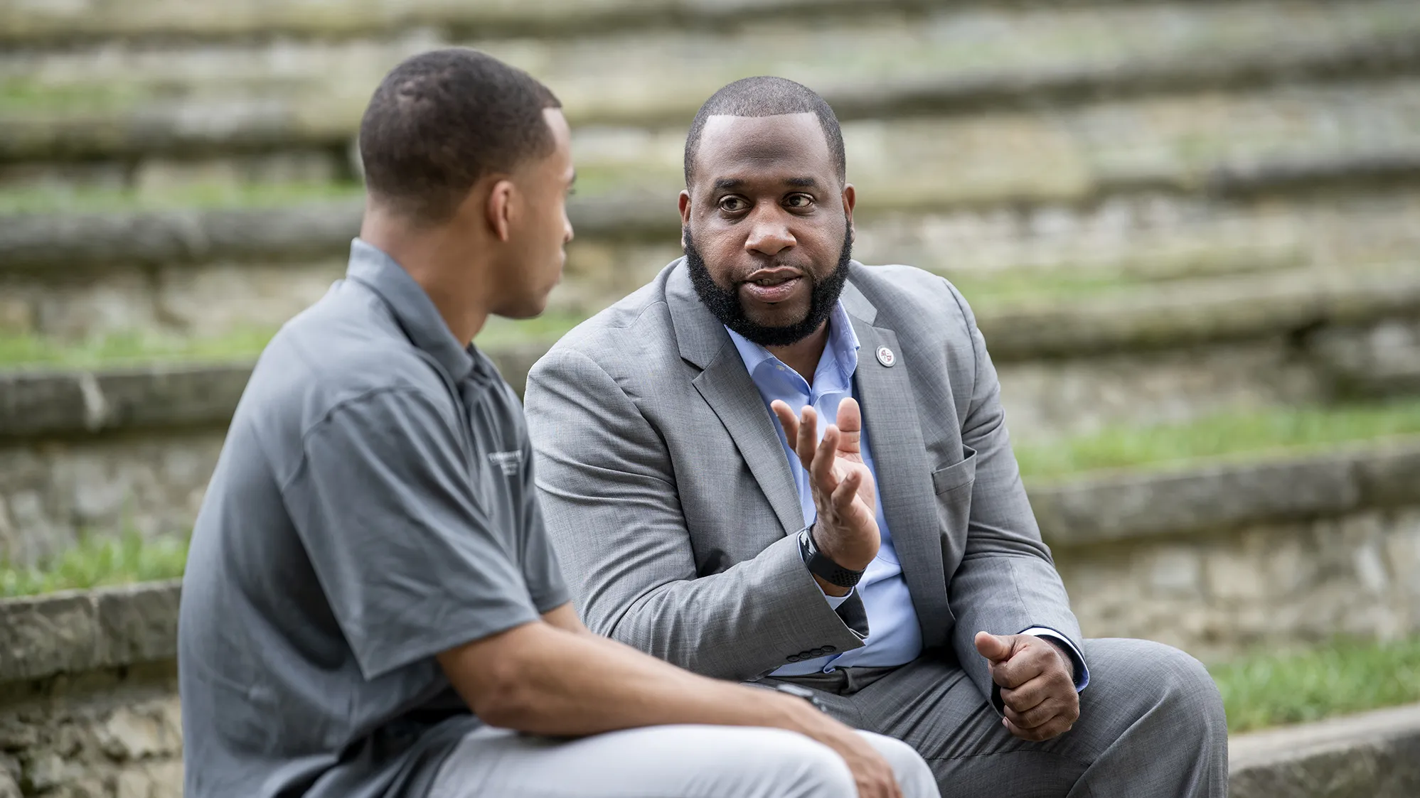 Dan Thomas, a Black man with neatly trimmed hair and beard, gestures as he looks directly at student Mike Hull, a young Black man looking away from the camera as he meets Thomas’ eyes. They look like they’re having a meaningful conversation.