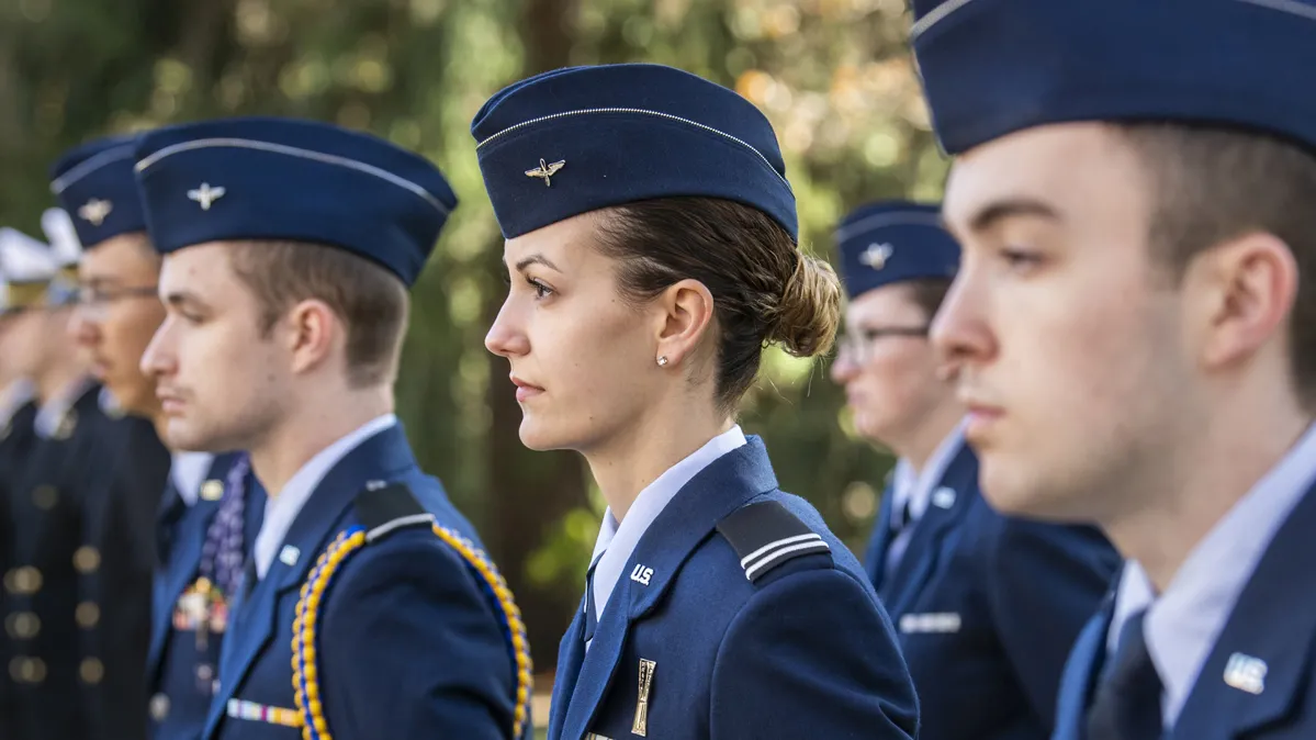 ROTC students at Ohio State stand in a line at attention in their uniforms and hats. They’re outside on an early fall day when the sun is shining brightly.