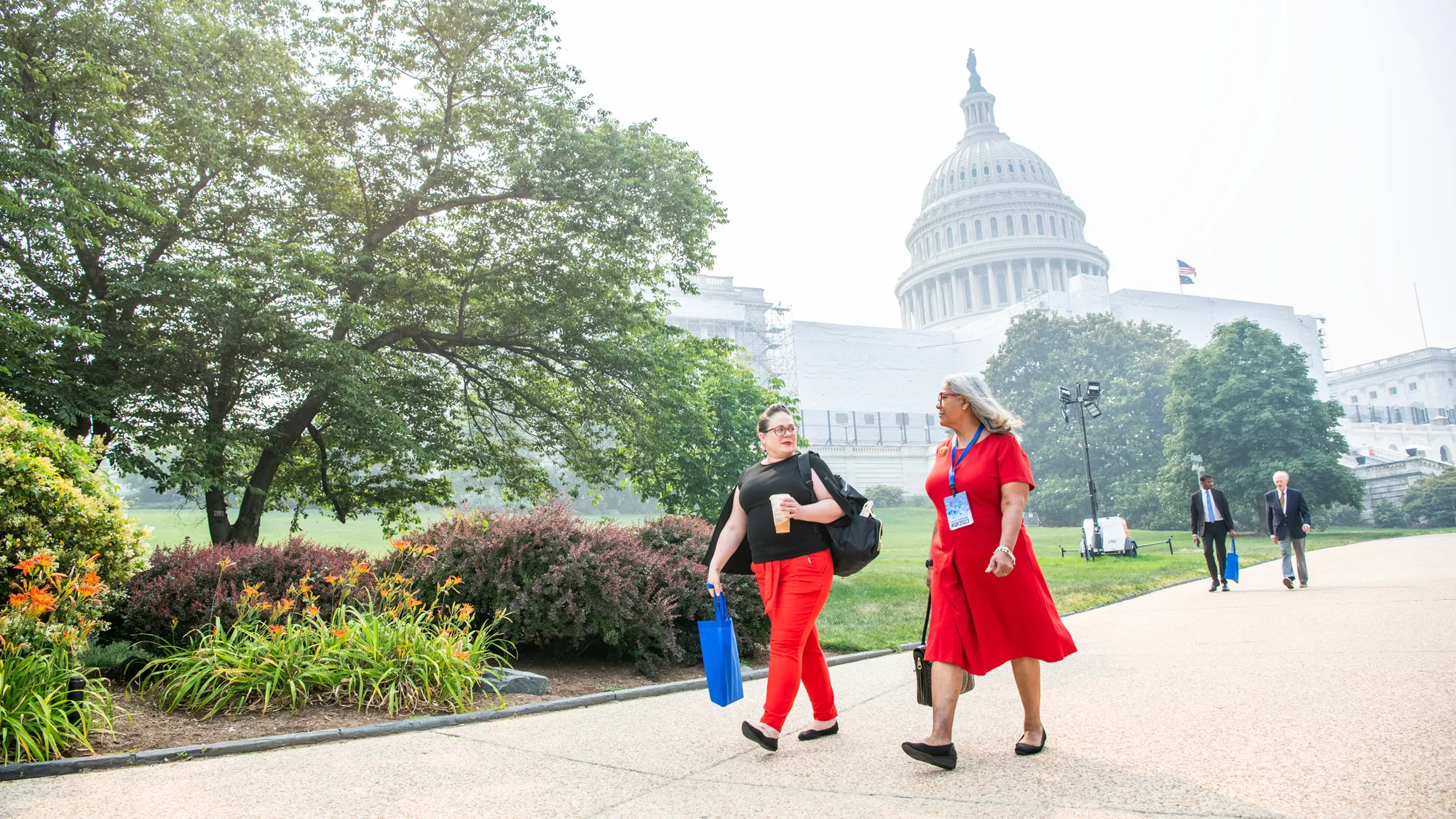 Carrying a coffee and a couple of tote bags, Gretchen Klingler walks outside the U.S. Capitol building with an older woman whose gray hair is blowing behind her. They’re looking at each other, both through red glasses that match the woman’s dress and Gretchen’s pants. The day is hazy, making the sky look only a slightly lighter shade than the capitol dome. 