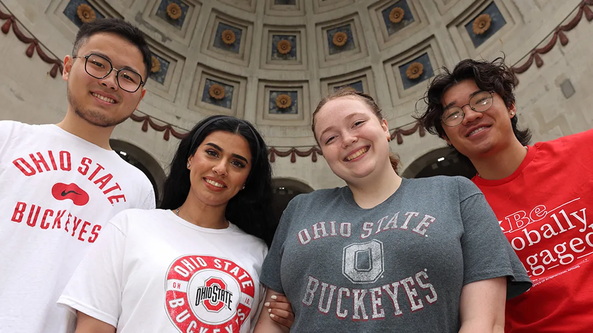 Four Buckeyes wearing Ohio State T-shirts grin as they stand in the rotunda of Ohio Stadium