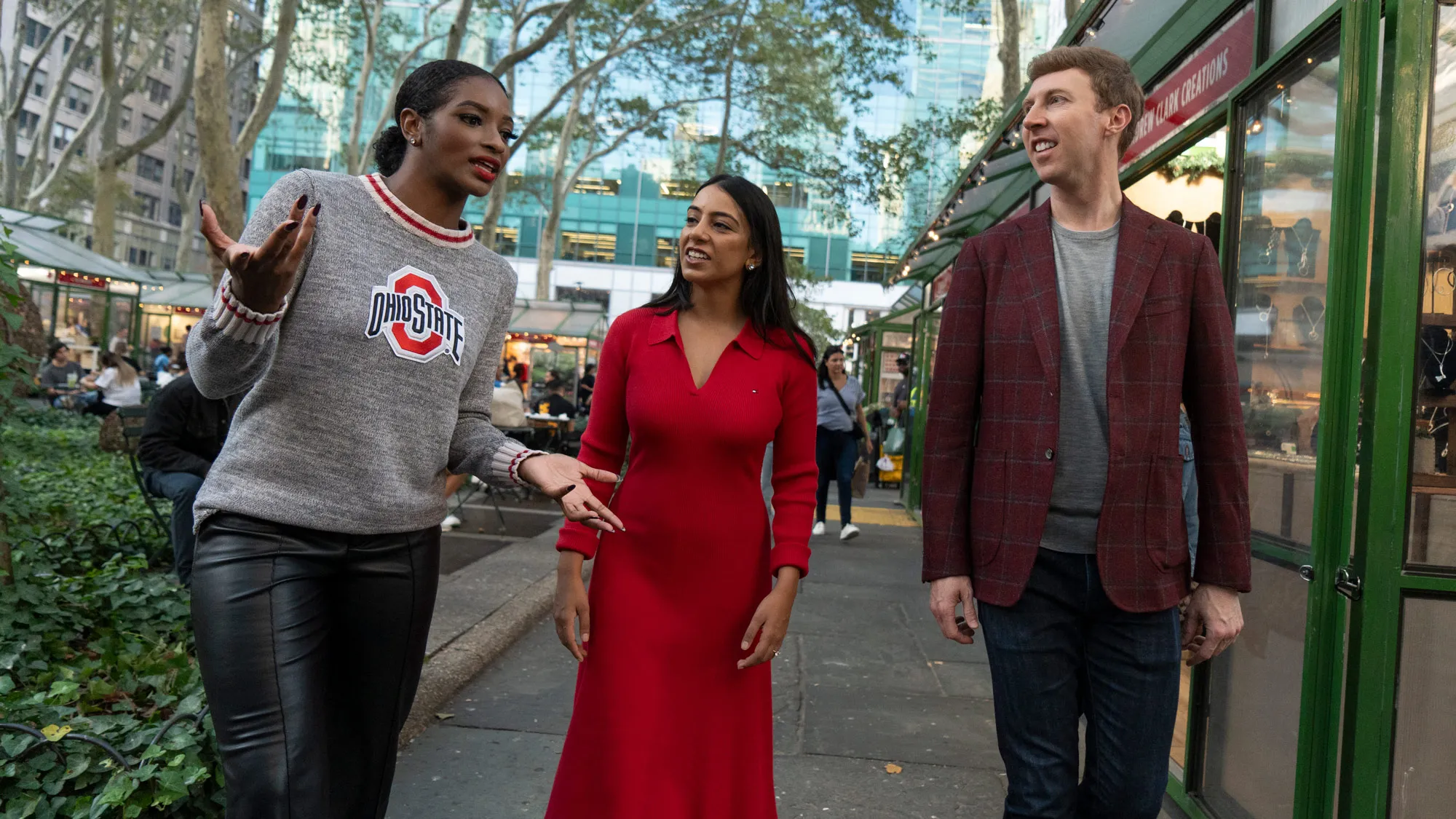 Three Buckeyes chat as they happily walk up a New York City street sidewalk wearing Buckeyes gear or colors.