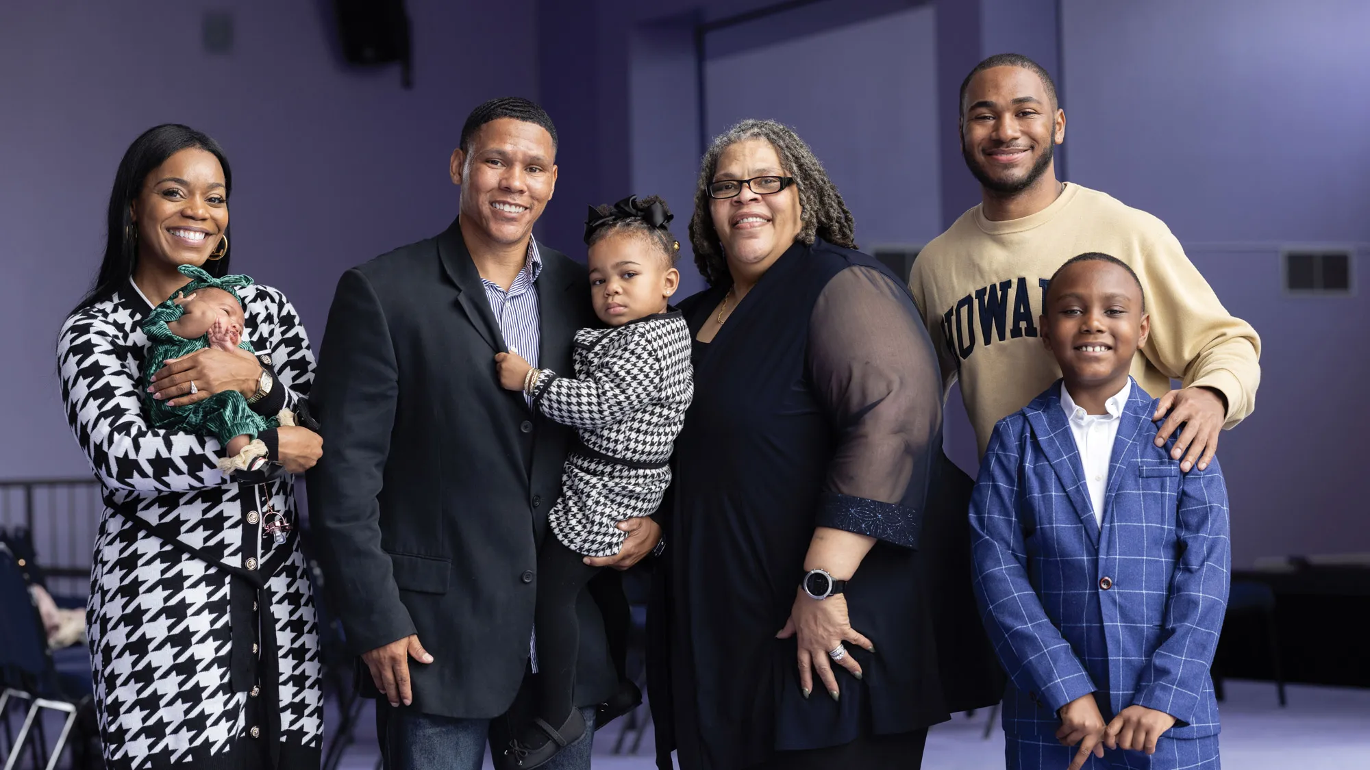 Patrice Palmer poses with one of her sons, Brandon Palmer, and his family. From left are his wife, a pretty woman with long hair wearing a black and white dress and holding a baby dressed in green; Brandon, who wears a sports coat and dark jeans and holds a young daughter wearing an outfit similar to her mom’s; Patrice, in a pretty top with see-through sleeves; Brandon’s oldest son, a two-time Howard graduate wearing a sweatshirt from his alma mater; and Brandon’s youngest son, who wears a snazzy blue check