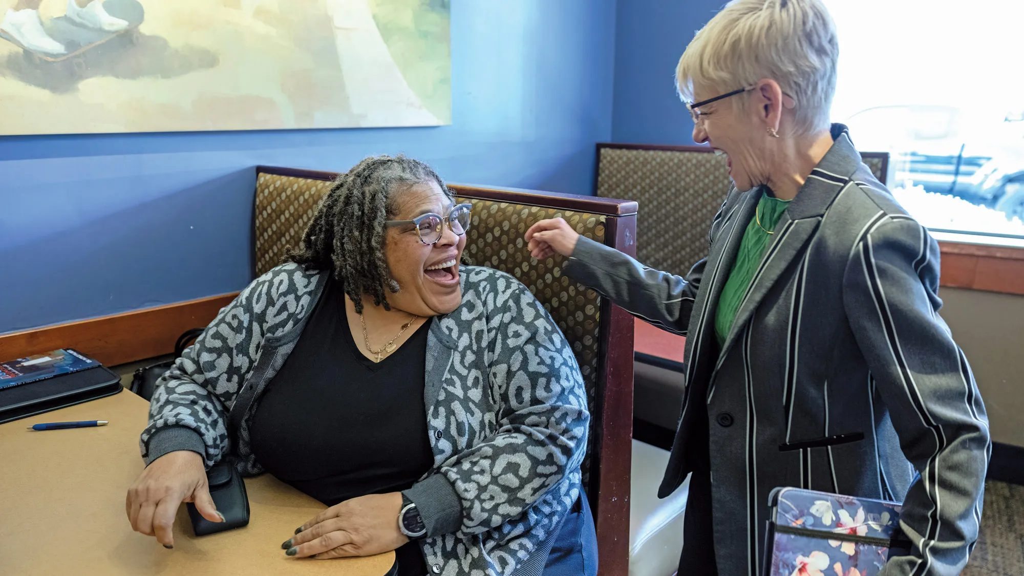 Patrice Palmer pivots as she sits in a restaurant booth to greet a friend just arriving for a meeting. Both women seem sincerely happy to see each other, as they’re making eye contact with wide grins.