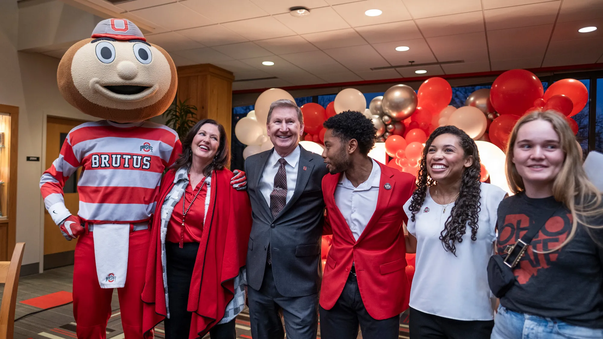 From left, Brutus Buckeye, First Lady Lynda Carter and President Carter, Undergraduate Student Government leaders Bobby McAlpine and Madison Mason, and another young woman line up at a student welcome reception in the Union. They have their arms wrapped around each others’ shoulders and are all laughing.