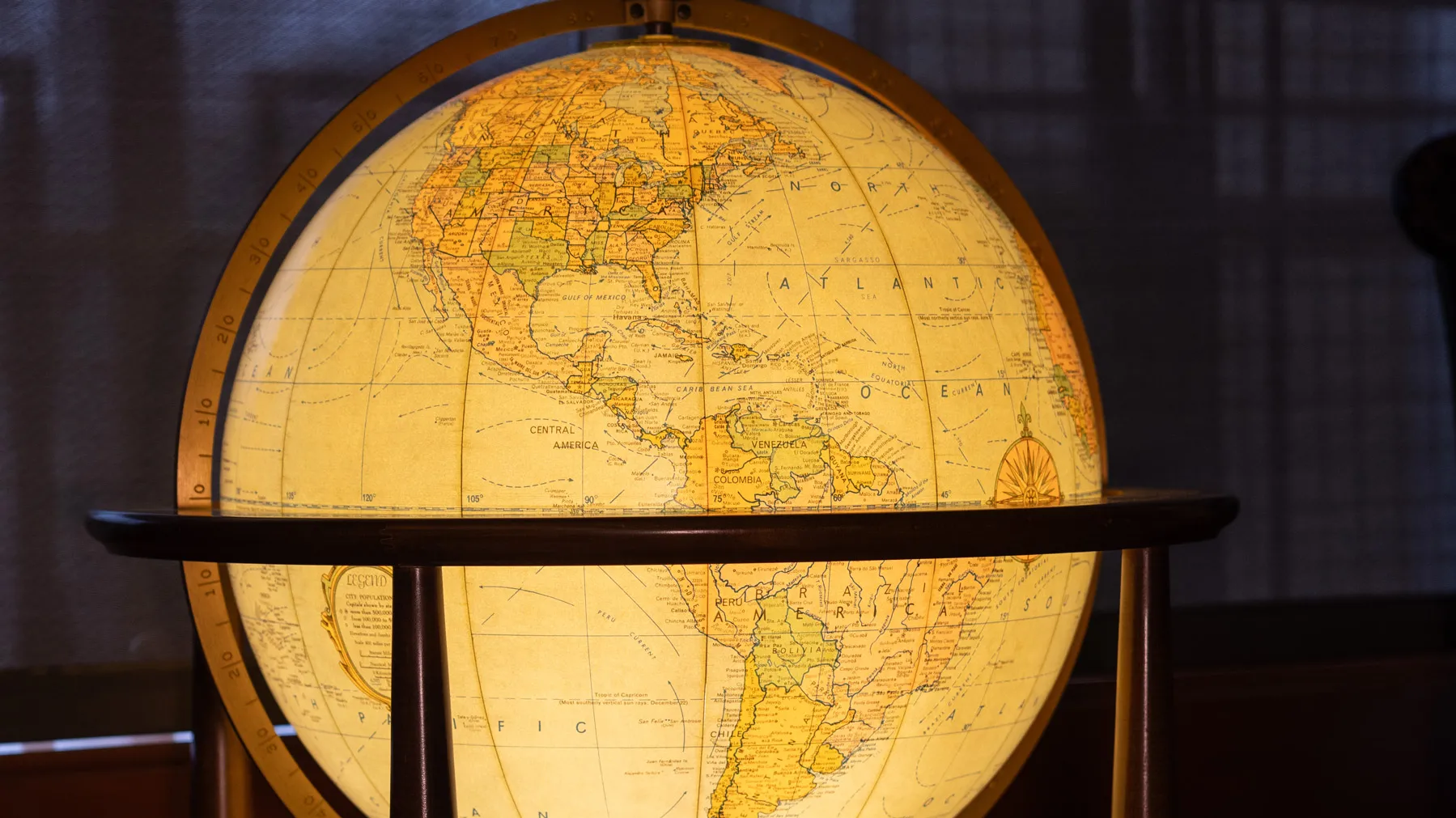 A lighted-up globe, positioned to show North and South America is held in a simple wooden stand. They background of the photo is dark, so the globe shines brightly.