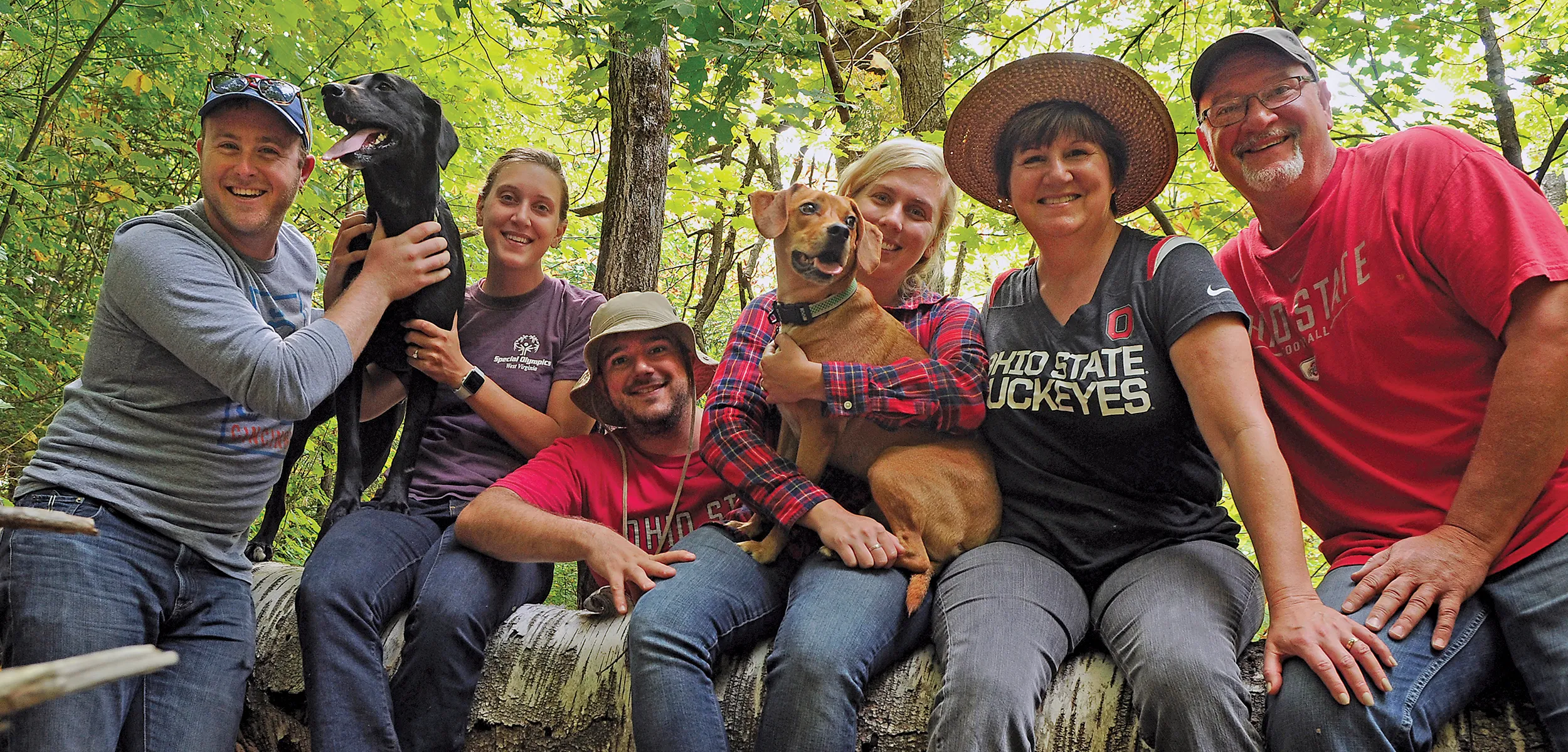 Sitting on a low wall on a hiking trail in the woods, Mary Alice Casey and her family pose with their pets. Both of her grown children and their spouses brought their dogs for their hike, and her husband, an alumnus, wears an Ohio State T-shirt. The whole family looks like they’re enjoying themselves.