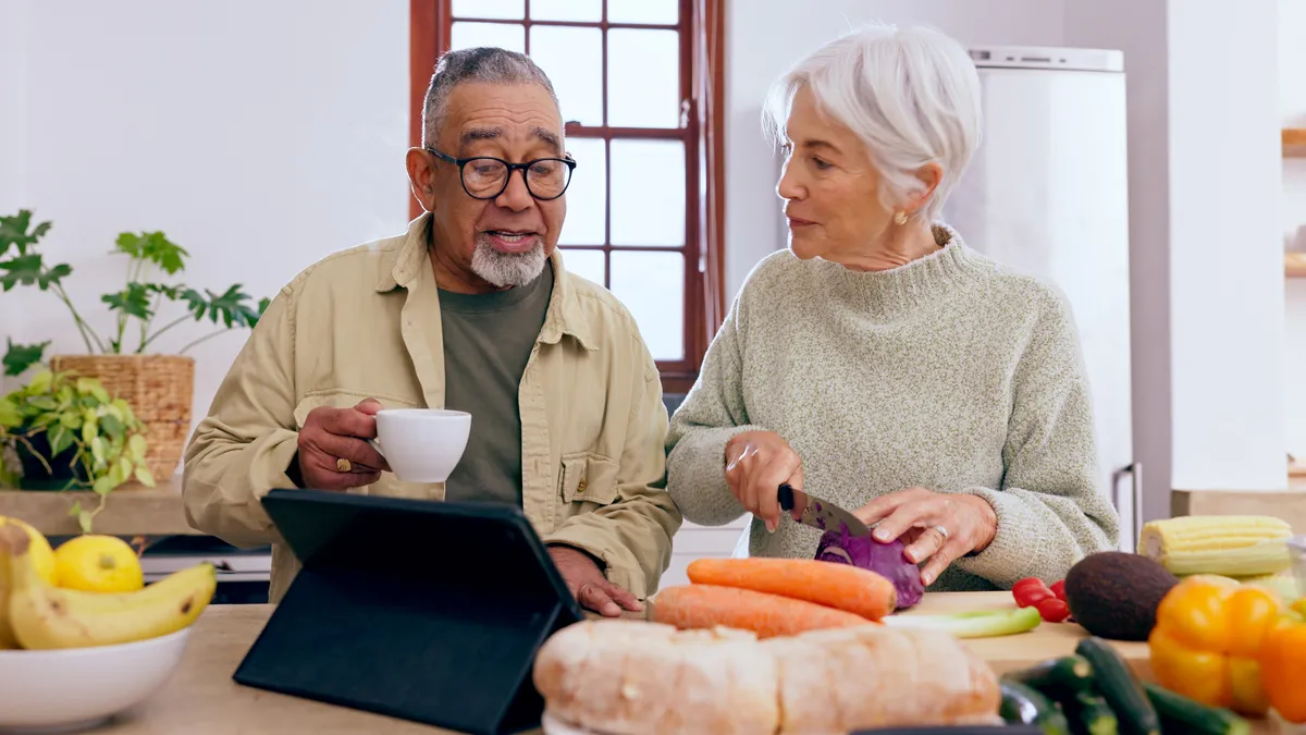 A senior couple prepares a healthy meal with a variety of vegetables and fruits in view