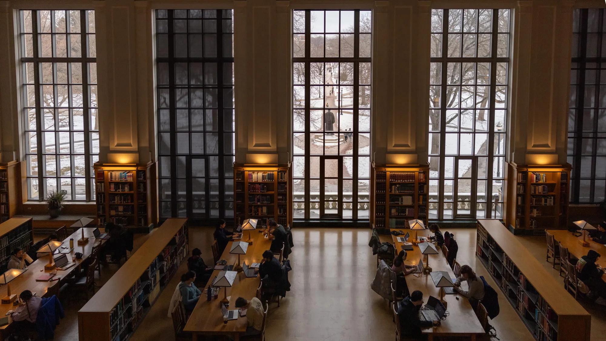 This photo, taken from high above students studying hard at long tables, shows—through tall windows—some the Oval’s iconic paths driving through the snow-covered grass sections. The light from the windows reflects off the floor and lamps here and there glow. 