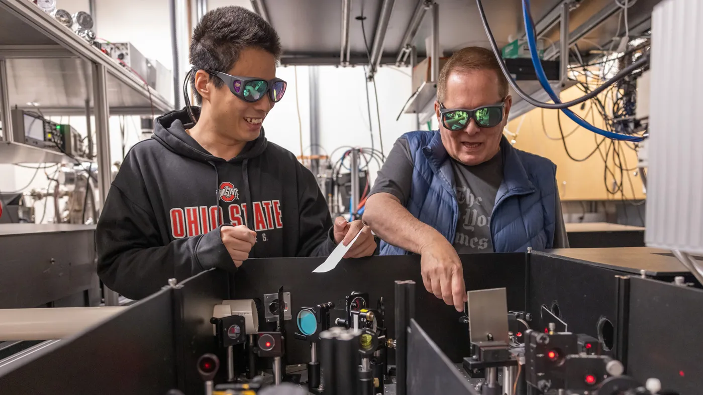 Lou DiMauro and a student, postdoc Yaguo Tang from China, wear safety glasses as they point out how a laser is split into two for their attosecond experiments to study electrons.
