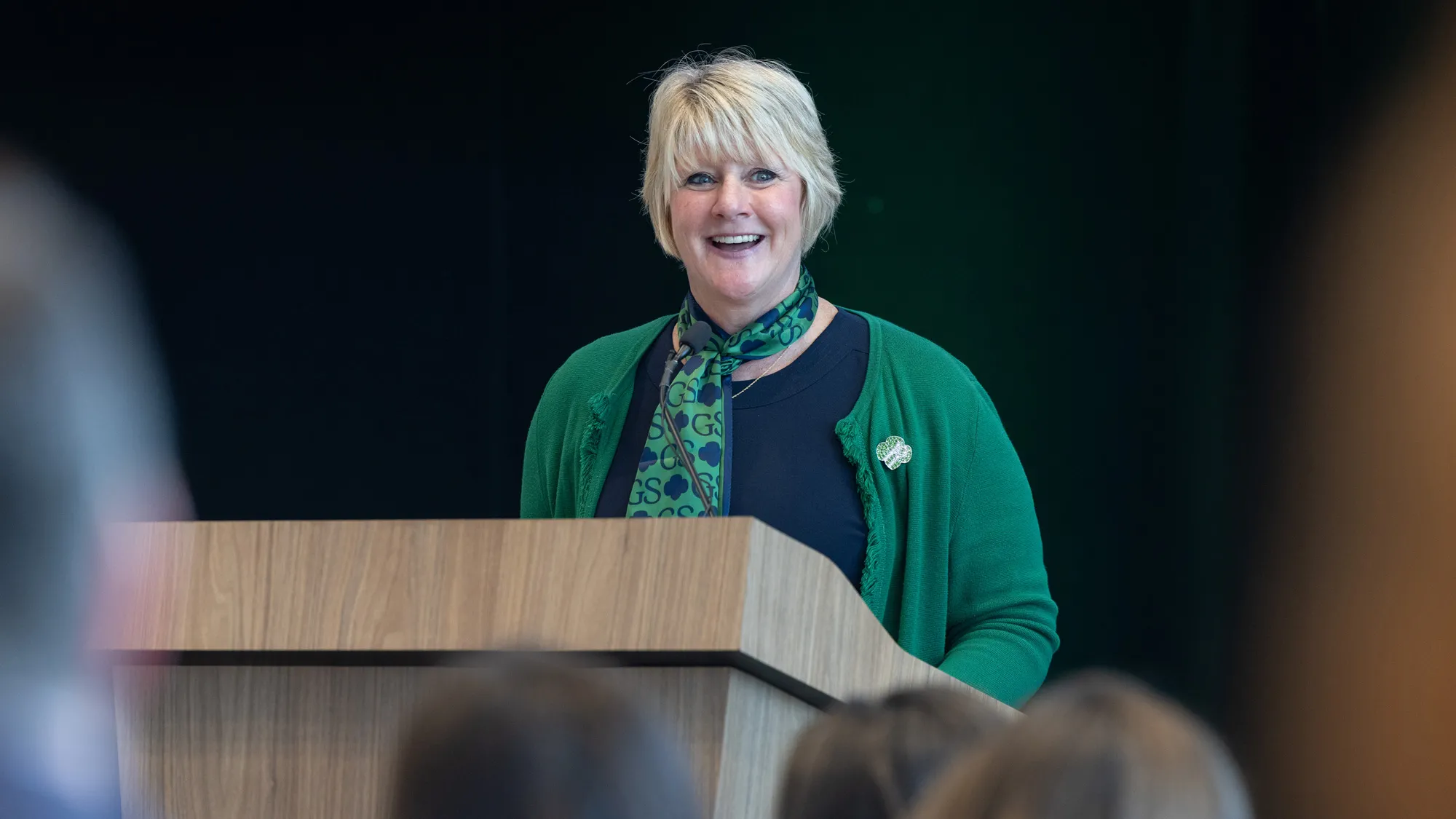 Wharton smiles as she speaks at a lectern to the crowd at the conference. She seems confident and comfortable being in the lead position. 