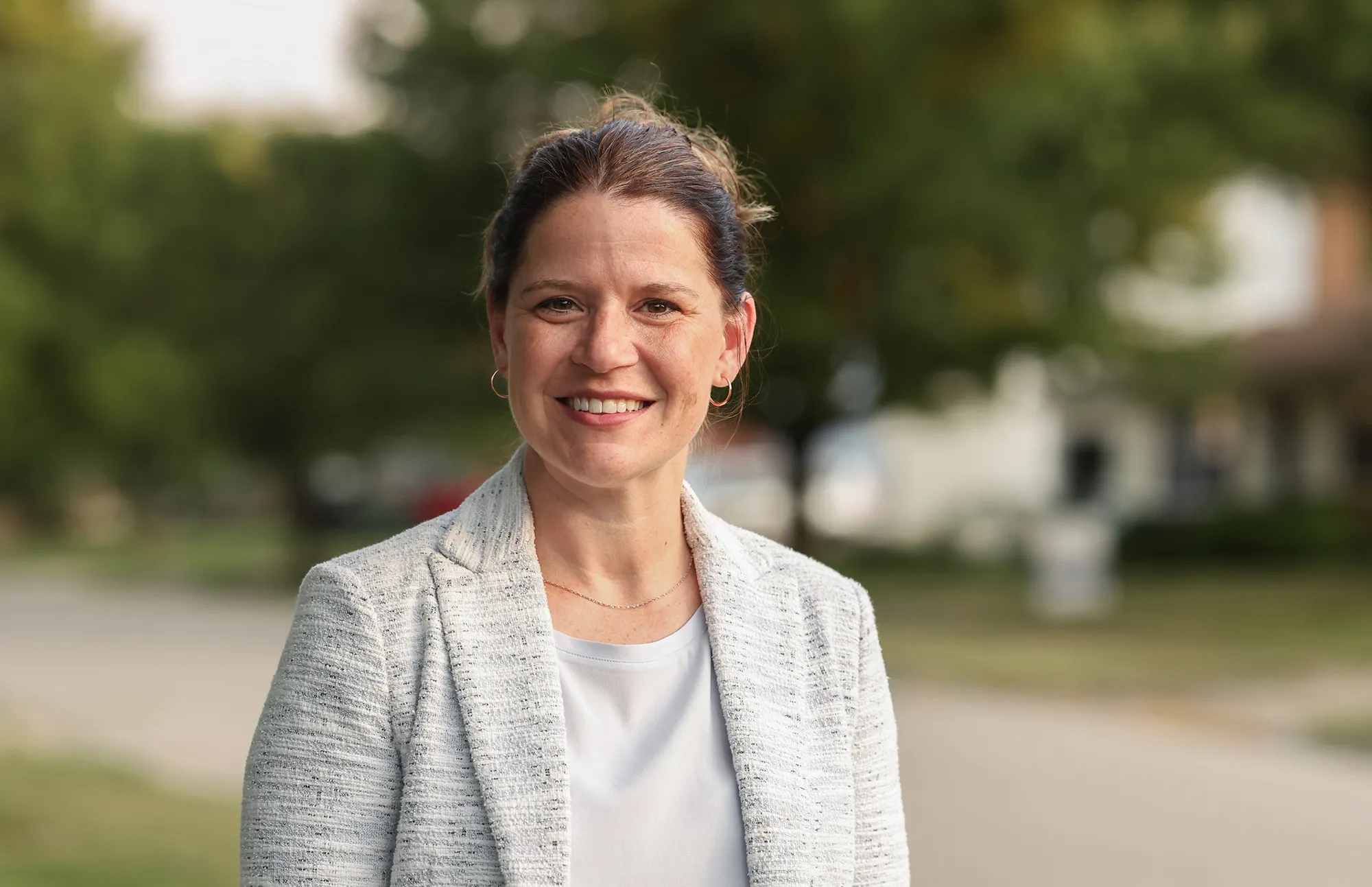 Stephanie Mouton, a friendly-looking brunette with her hair pulled back, wears a sport coat over a T-shirt as she poses on a street with houses for sale. She’s a white woman who looks younger than she probably is given her expertise and knowledge base.